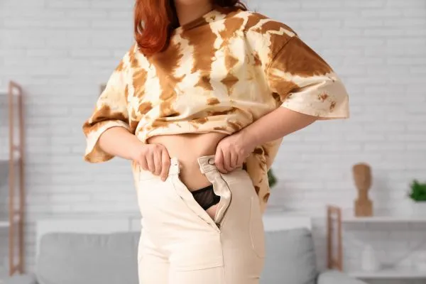 Image of woman trying to do her trousers up after pregnancy weight gain Moseley