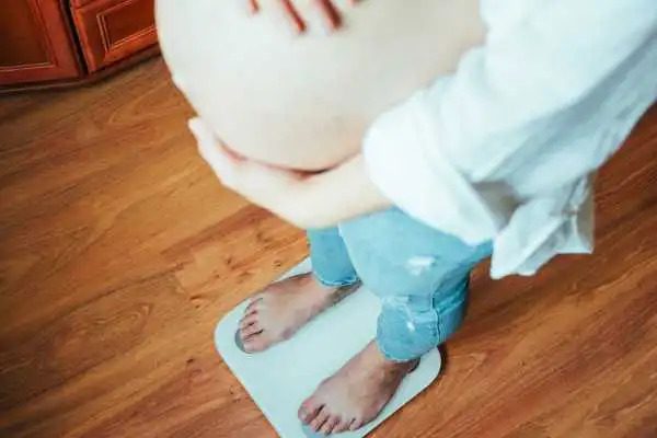 Image of woman weighing herself and experiencing weight gain through pregnancy Moseley